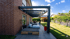 Moderne Pergola aus Metall an einem roten Backsteinhaus mit Liegen und Garten.