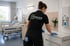 Reinigungskraft in schwarzer SCHULDIS Uniform reinigt eine Kommode in einem Patientenzimmer.