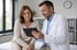 Arzt im weißen Kittel zeigt einer Patientin Informationen auf einem Tablet in einer Praxis.