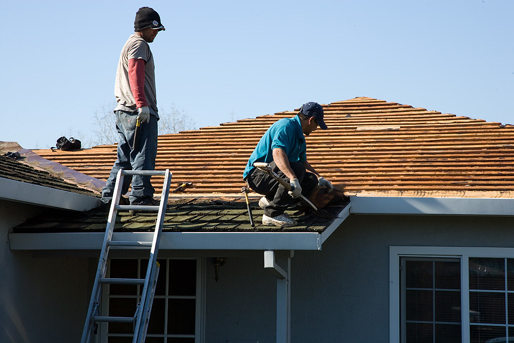 Roofing crew working on a stripped roof deck beside a ladder