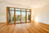 Helles, leeres Zimmer mit Parkettboden und großer Glasfront aus Holzrahmen, die auf einen Balkon mit Stadtblick führt.