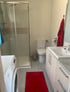 Modernes Badezimmer mit Glasdusche, weißer Toilette, Waschbeckenunterschrank, Waschmaschine und rotem Teppich.