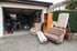 Sperrmüll wie Sofa, Sessel, Matratze und Teppichrolle steht vor einer vollgestellten Garage zur Abholung bereit.