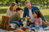 Eine vierköpfige Familie macht ein Picknick im Park auf einer Decke mit Korb, Erdbeeren und Gebäck.