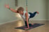 Eine Frau führt die Yoga-Übung Bird-Dog auf einer Matte in einem Studio mit Chakra-Symbolen im Hintergrund aus.