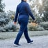 A person in a blue tracksuit walks along a gravel path in a park.
