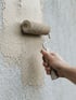Eine Hand streicht eine strukturierte Wand mit einer Farbrolle in beiger Farbe.