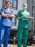 Zwei Krankenschwestern in blauer und grüner Uniform stehen vor einem modernen Gebäude.