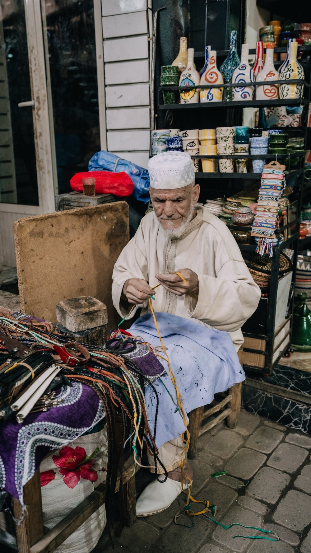 Älterer Händler in heller Djellaba knüpft Schnüre in seinem Laden