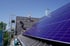 Zwei Installateure montieren dunkelblaue Solarpaneele auf einem schrägen Dach mit Ziegeln.