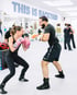 Eine Frau mit rosa Boxhandschuhen und ein Mann trainieren lachend Boxen im Boxstudio „This is Backyard“.