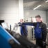 Zwei Männer in blauen Arbeitsjacken bedienen Maschinen in einer Fabrikhalle.