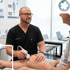 A male doctor performs an ultrasound on a patient's knee in a clinical setting.