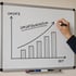 Hand zeichnet ein Balkendiagramm zum Umsatzwachstum auf ein Whiteboard mit aufsteigender Trendlinie.