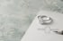 Ein Verlobungsring mit großem Diamanten im Halo-Schliff und ein passender Vorsteckring mit Diamantbesatz auf grauem Grund.