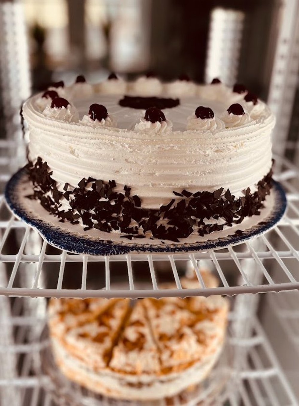 Schwarzwälder Kirschtorte mit Sahnetupfen, Kirschen und Schokoladenspänen in der Kühlvitrine