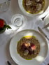 Zwei Schüsseln mit Risotto und Pilzen auf einem weißen Tisch, daneben Wassergläser und Besteck.