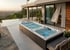 Ein großer Swim-Spa mit Sprudelfunktion und Whirlpool auf einer Terrasse vor einem Haus mit Pool und Landschaft.