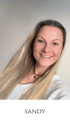 Eine blonde Frau mit schwarzer Halskette lächelt in die Kamera. Der Text "SANDY" steht unten.