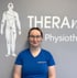 Eine lächelnde Frau mit Brille und blauem T-Shirt mit "THERAMOVE" Logo vor einer Wand mit Text "THERAMOVE Physiotherapie".