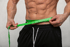 Muscular man with visible abs measuring his waist with a green tape measure over black athletic shorts.