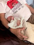 Ein schlafendes Neugeborenes liegt im Arm eines Mannes mit T-Shirt-Aufdruck „Opa ist da!“.