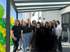 Eine Gruppe von 14 Personen, lächelnd vor einem modernen Gebäude mit Ballons in Grün und Gelb.