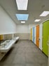 Sauberer Toilettenraum mit bunten Kabinentüren, langen weißen Waschbecken und Spiegeln.
