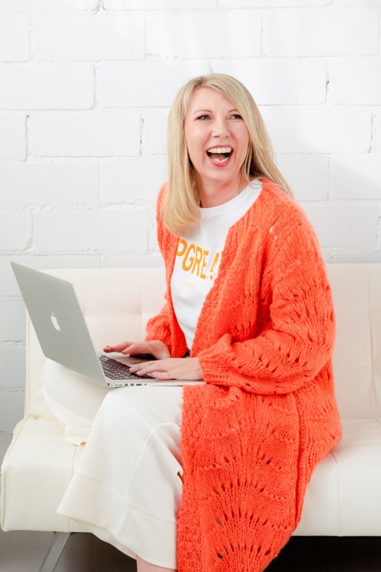 Susanne Kettler lachend mit Laptop auf dem Sofa