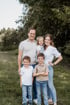 Eine fünfköpfige Familie lächelt stehend auf einer Wiese vor Bäumen in heller Freizeitkleidung und Jeans.