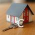 Modellhaus mit rotem Giebel, grauer Dachfläche, weißer Fassade und einem Schlüssel mit Euro-Anhänger auf Holztisch.