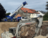 Ein weißer Bagger und ein blauer Weiss Kranservice Kran auf einer Baustelle mit Schutt.