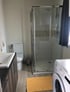 Modernes Badezimmer mit Toilette, Waschbecken, Glasdusche, orangefarbener Badematte und Waschmaschine.