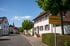 Gelbes Ortsschild von Büttelborn an einer sonnigen Straße mit Wohnhäusern und Bäumen unter blauem Himmel.