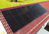 Schwarze Solarpaneele auf einem roten Ziegeldach eines Hauses mit grüner Wiese im Hintergrund.