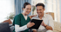 A smiling female nurse in green scrubs shows a tablet to a happy male patient in a white shirt.