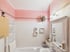 Badezimmer mit rosa Wänden, weißen Fliesen, einer Badewanne, einem Wandspiegel in Vintage-Optik und einem Handtuchheizkörper.