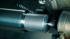 Eine CNC-Maschine dreht Gewinde in ein Metallrohr, während Metallspäne abfallen.