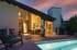 Hinterhof mit beleuchtetem Pool, Feuerstelle, Lounge-Sesseln und Terrasse bei Sonnenuntergang.