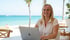 Lächelnde blonde Frau arbeitet am Laptop am Strand mit Palmen und blauem Meer im Hintergrund.