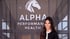 A woman stands in front of a glass wall featuring the Alpha Performance Health logo and a white horse head icon.