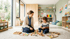 Erzieherin und Kind spielen gemeinsam mit Holzbausteinen auf einem Teppich in einem hellen Montessori-Kinderzimmer.