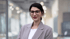 Eine junge Frau mit Brille und dunklem Rollkragenpullover, die mit verschränkten Armen lächelt.