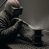 Eine Person in Schutzkleidung sandstrahlt ein Metallteil auf einer perforierten Oberfläche.
