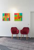Zwei rote Samtstühle unter farbenfrohen abstrakten Bildern in einem Wartezimmer mit weißen Türen.