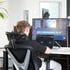 Ein Mann sitzt in einem ergonomischen Bürostuhl an einem Schreibtisch und bearbeitet Videos am Monitor und Laptop.