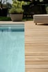 Modernes Schwimmbecken mit hellblauem Wasser direkt neben einer Terrasse aus schmalen Holzbohlen.