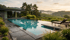 Rechteckiger Pool mit Liegestühlen, dahinter ein modernes Gebäude, Weinberge und bewaldete Hügel bei Sonnenuntergang.