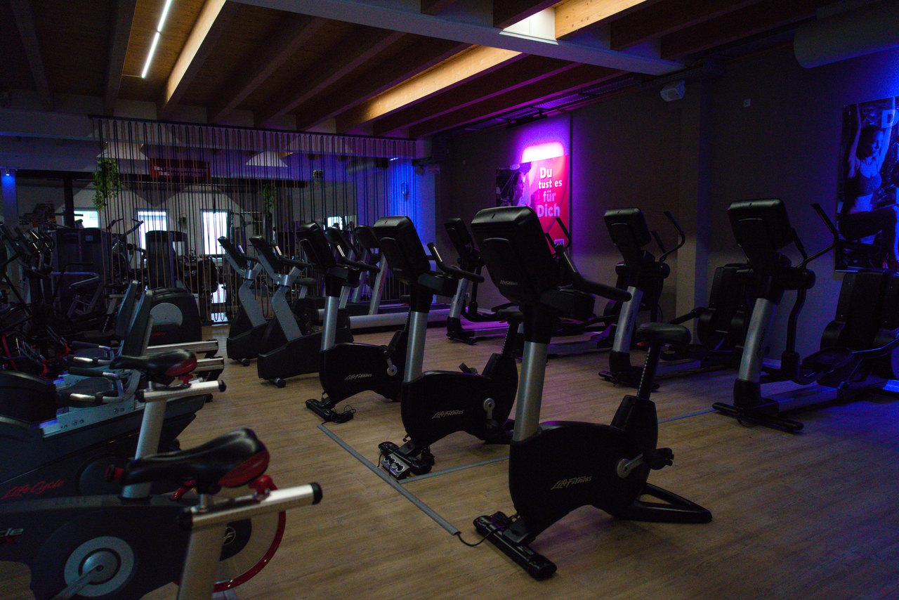 Reihe von Heimtrainern in einem Fitnessstudio mit Neonlicht.