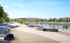 Riverside promenade with tiered seating, trees, distant stadium, and boats on the water under a clear sky.